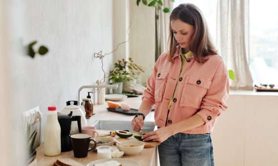 A woman slices an avocado in a bright, modern kitchen with natural light.